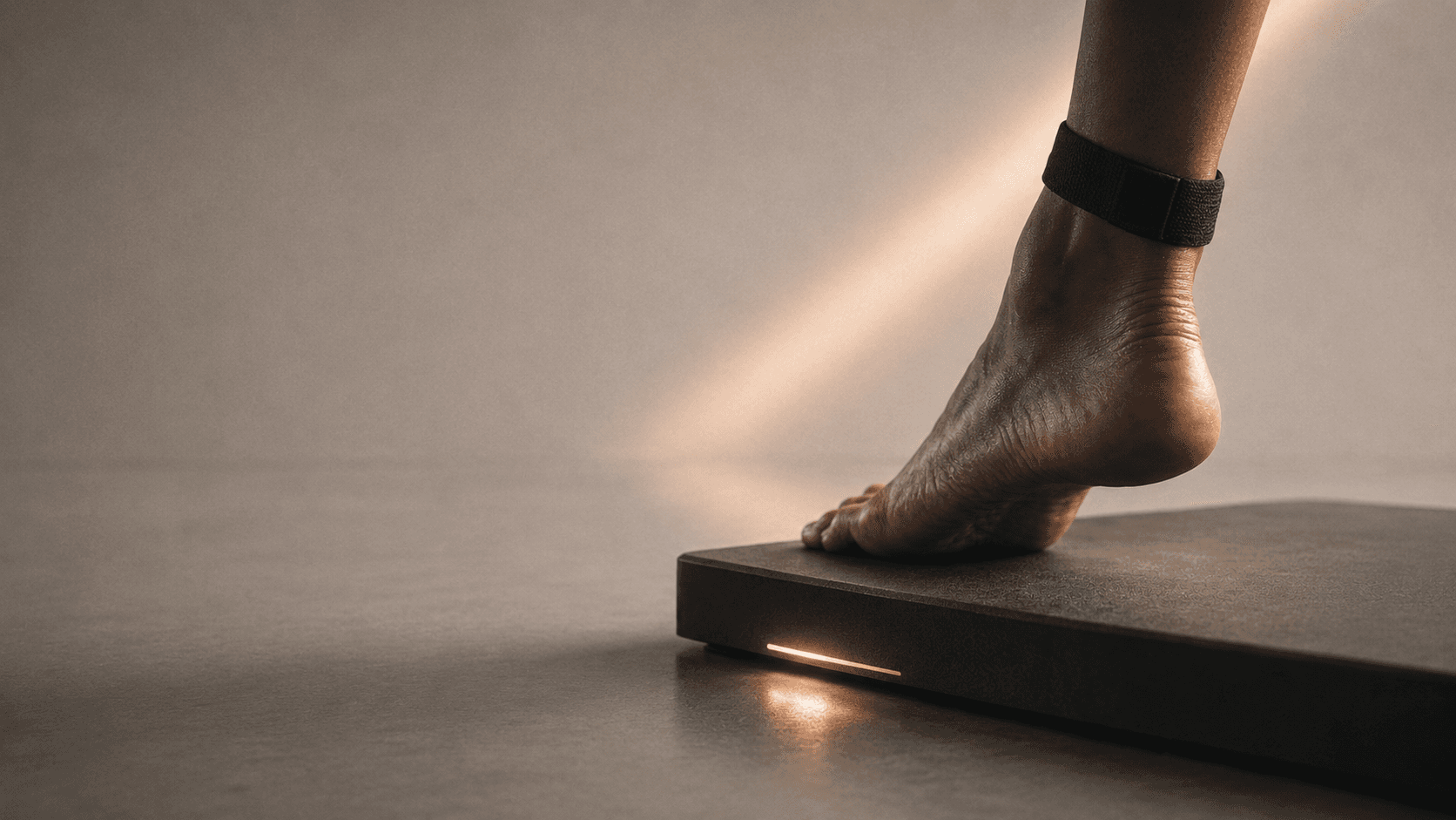 Bare foot stepping onto a force-measurement platform, sport wearable on the ankle, lit by a single warm beam.